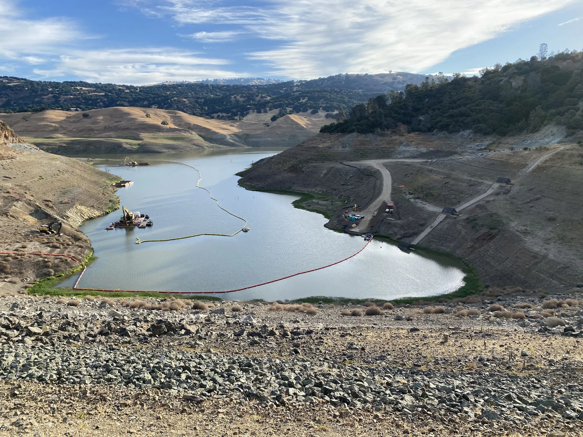 Reservoir behind an earthen dam with floating work barges and turbidity booms